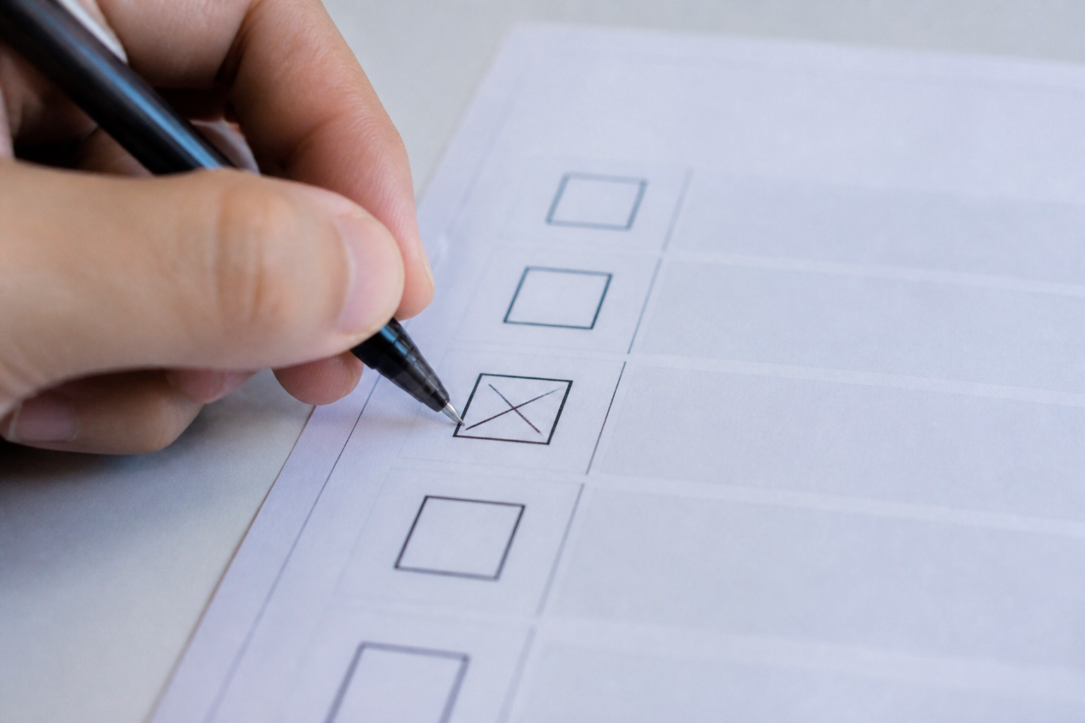 A hand marking a paper ballot with a pen.